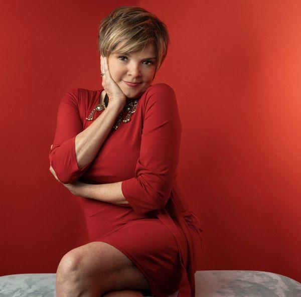 Publicity portrait of jazz vocalist Karrin Allyson, smiling and posing in a red dress against a matching red background.